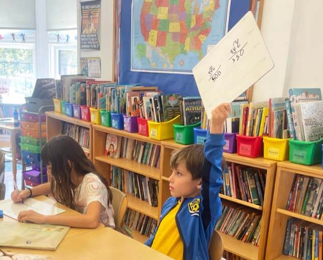 Lower School math classroom student raising work board